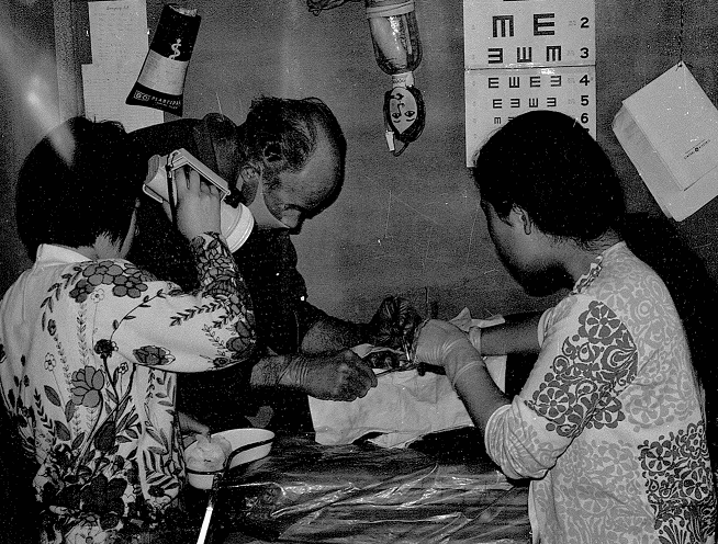 Black-and-white photo of a man believed to be Dr. John R. Sibley conducting a dental exam, assisted by two nurses holding instruments.