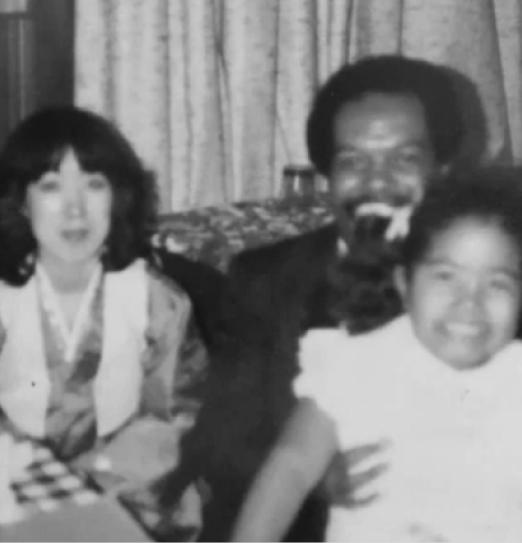 Two people smile closely together at an indoor gathering, captured in a soft black-and-white photograph.