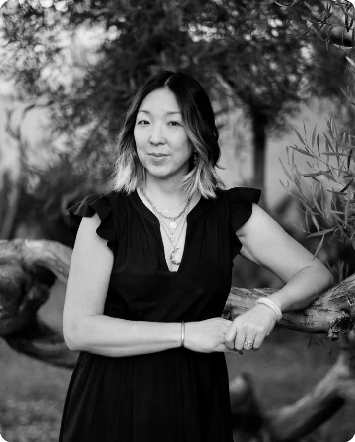 Katherine Yungmee Kim stands outdoors in a dark dress with her hair pulled back, looking toward the camera.